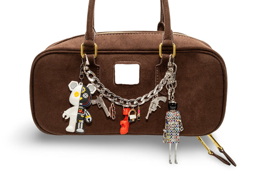 A brown handbag with custom-made chain charms attached to it. The charms include a small stuffed toy, a keychain, and other decorative items.
